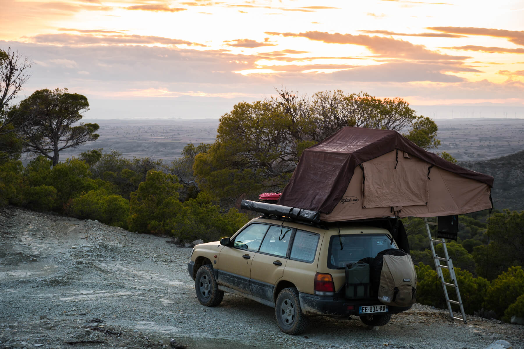 an overland subaru forester with a roof tent and a sunset